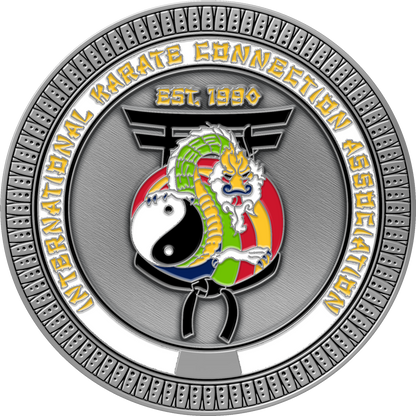 A circular silver-toned medallion or coin featuring the International Karate Connection Association logo and text, with a stylized dragon, yin-yang symbol, and martial arts motifs on a textured gray background.